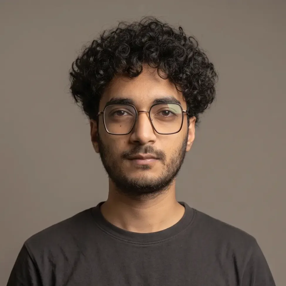 Muntaser Muttaqi, wearing glasses and a dark shirt, against a plain grey backdrop